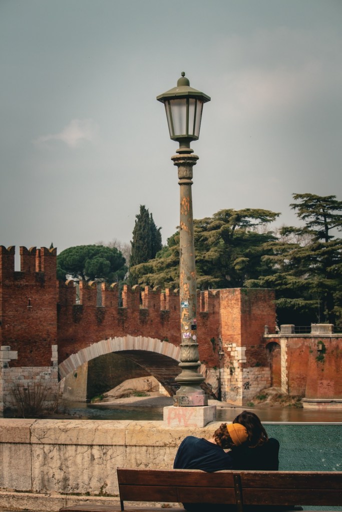 A couple sitting along the Adiga River at the Castelvecchio in Verona, Italy, March 2024